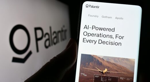 A hand holding a phone in front of a Palantir logo